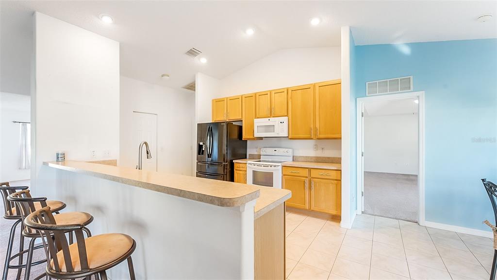 A kitchen features light wood cabinets, a black refrigerator, and a breakfast bar with stools — 8 WHITE HURST LANE, PALM COAST, FL