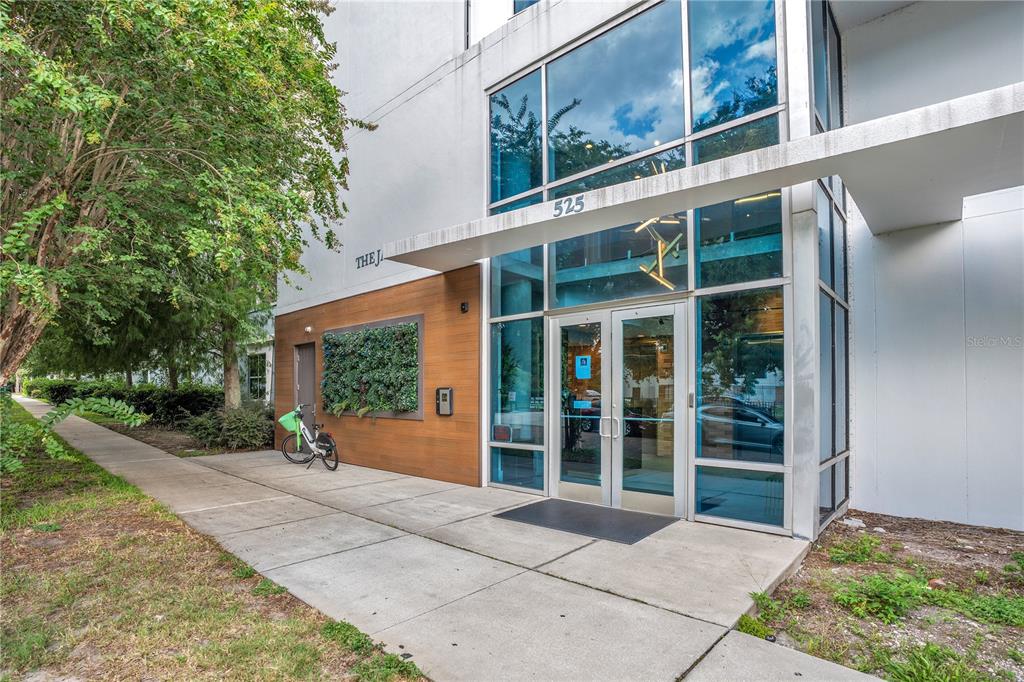 The exterior entrance of a modern building features glass doors, a wood-paneled wall, and landscaping — 525 E JACKSON STREET UNIT 308, ORLANDO, FL