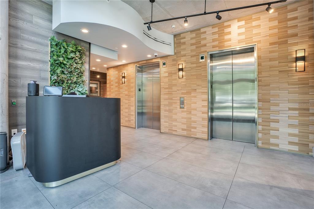A modern lobby features a black reception desk, two stainless steel elevators, and wood-paneled walls — 525 E JACKSON STREET UNIT 308, ORLANDO, FL