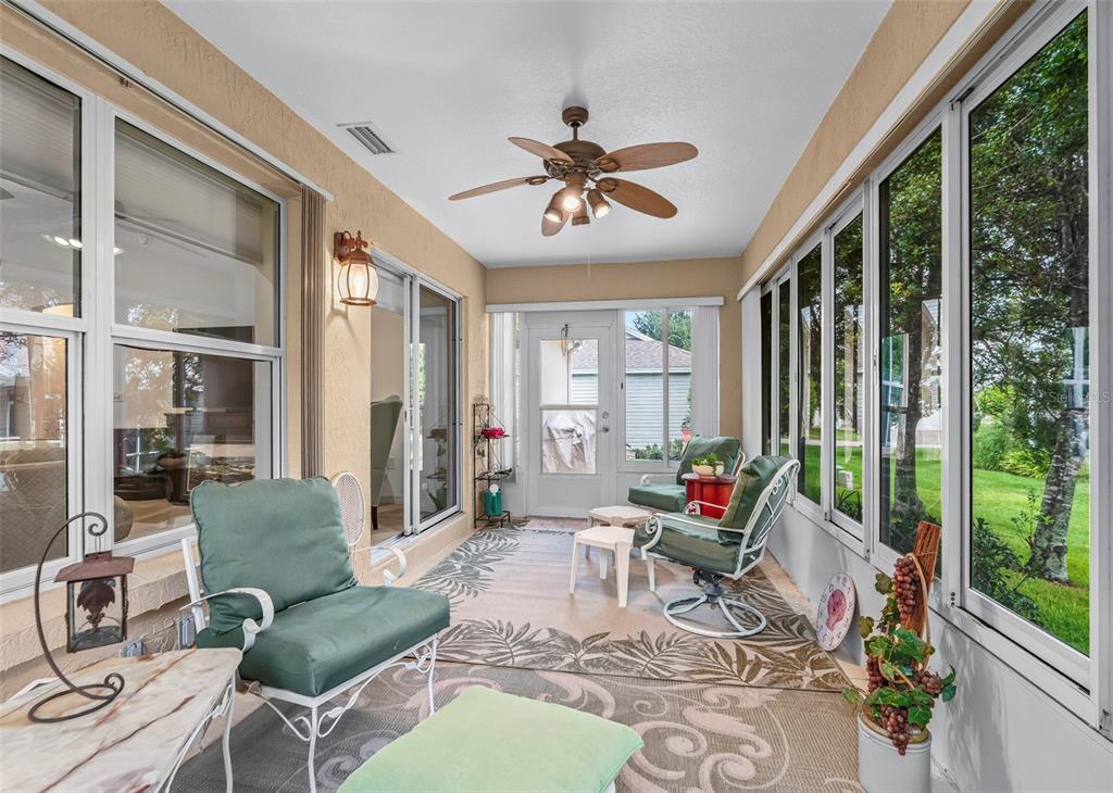 A sunroom features a ceiling fan, green cushioned chairs, a patterned rug, and large windows — 8368 SE 176TH LAWSON LOOP, THE VILLAGES, FL