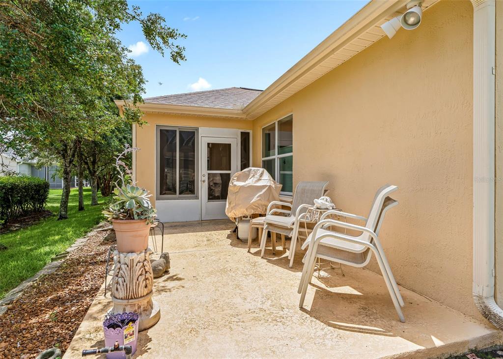 A concrete patio features a covered grill, two chairs, and a potted plant — 8368 SE 176TH LAWSON LOOP, THE VILLAGES, FL