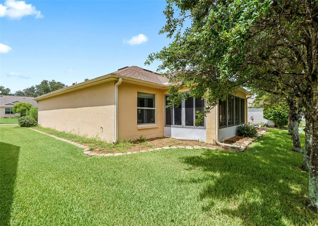 The exterior of a tan house features a screened-in porch and a large grassy yard — 8368 SE 176TH LAWSON LOOP, THE VILLAGES, FL