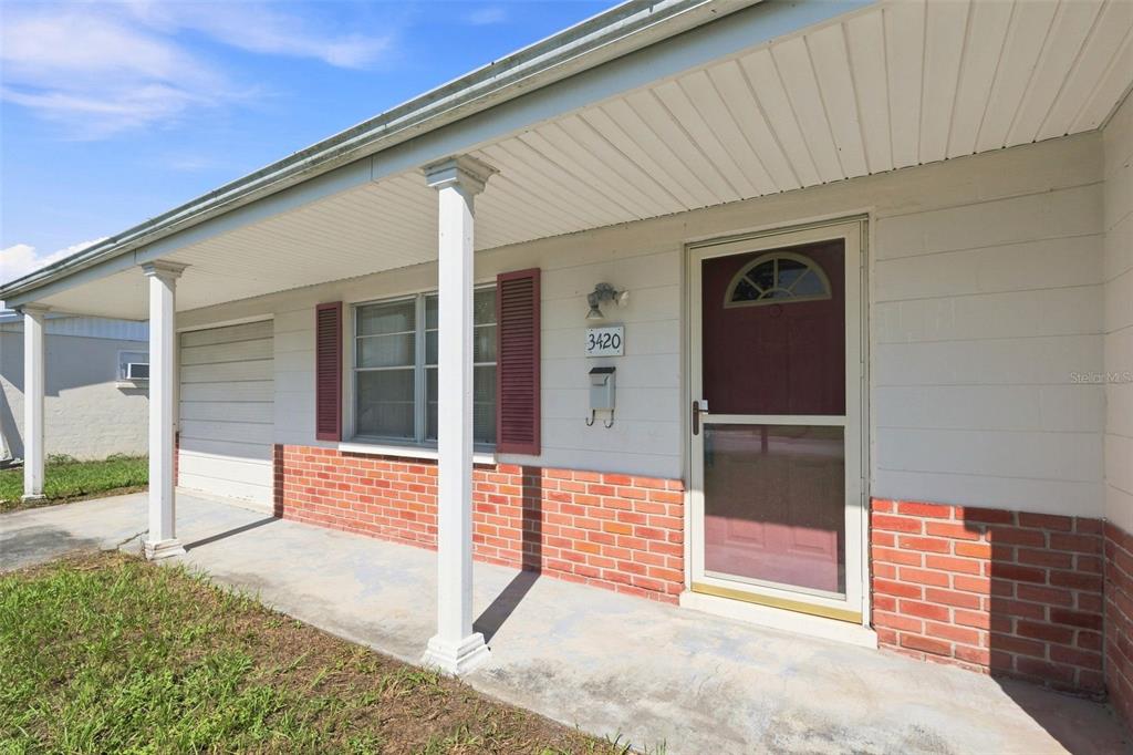 A single-story house exterior features a covered porch, brick accents, and a red front door — 3420 BLAYTON STREET, HOLIDAY, FL