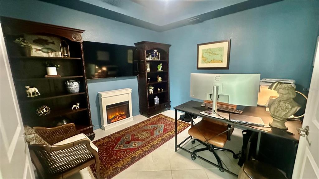 A home office features a desk, two bookcases, an electric fireplace, and a patterned area rug — 14221 HERITAGE LANDING UNIT 2013, PUNTA GORDA, FL