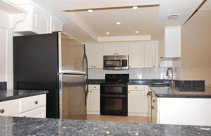 A kitchen features white cabinets, dark granite countertops, and black appliances — 8414 17TH STREET N, ST PETERSBURG, FL