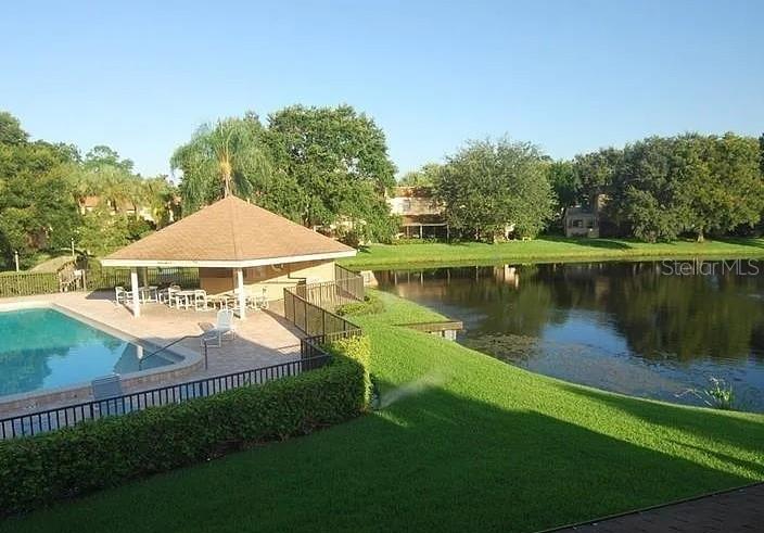A swimming pool and a covered pavilion sit beside a lake surrounded by green trees — 8414 17TH STREET N, ST PETERSBURG, FL