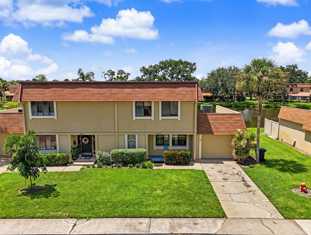 A two-story tan townhouse with a brown shingled roof sits beside a small pond — 8414 17TH STREET N, ST PETERSBURG, FL