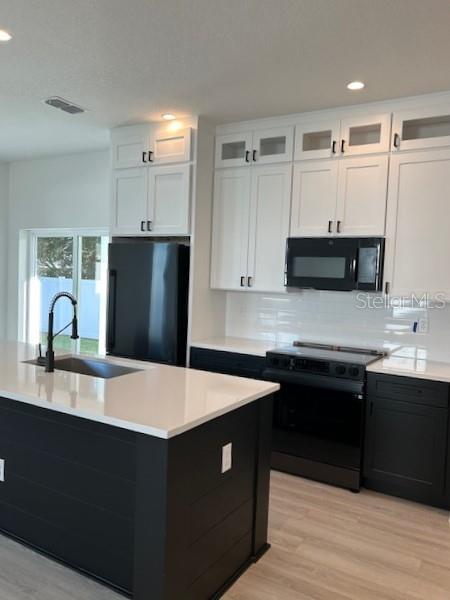 A kitchen features white upper cabinets, black lower cabinets, a central island, and stainless appliances — 2051 PEEL AVENUE, ORLANDO, FL