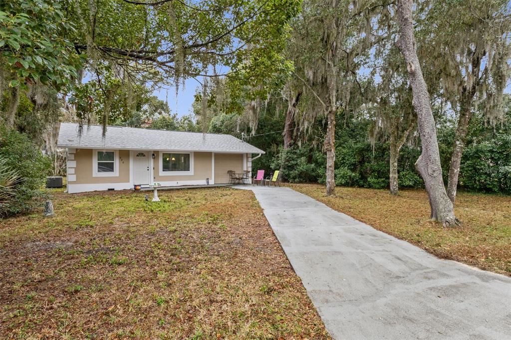 A single-story house with a concrete driveway sits among trees draped in Spanish moss — 690 E JACKSON AVENUE, MOUNT DORA, FL