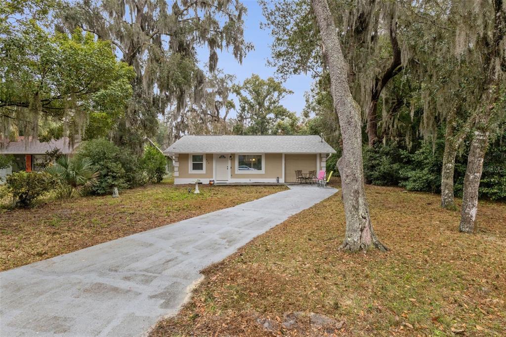 A single-story house with a concrete driveway sits among trees draped in Spanish moss — 690 E JACKSON AVENUE, MOUNT DORA, FL