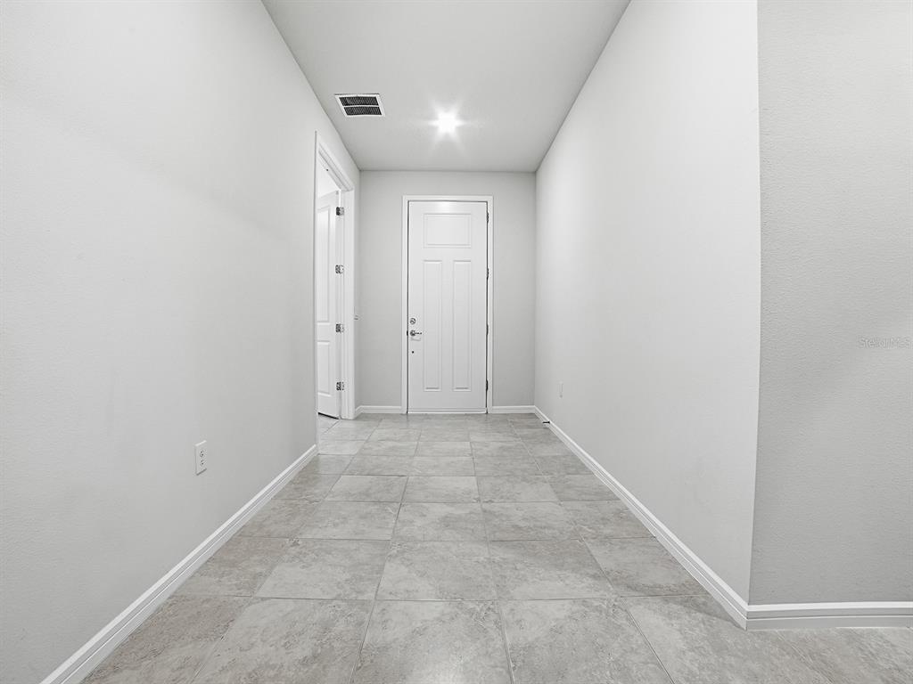 A hallway with light gray tile flooring leads to a white door and side entrance — 7771 SYRACUSE DRIVE, CLERMONT, FL
