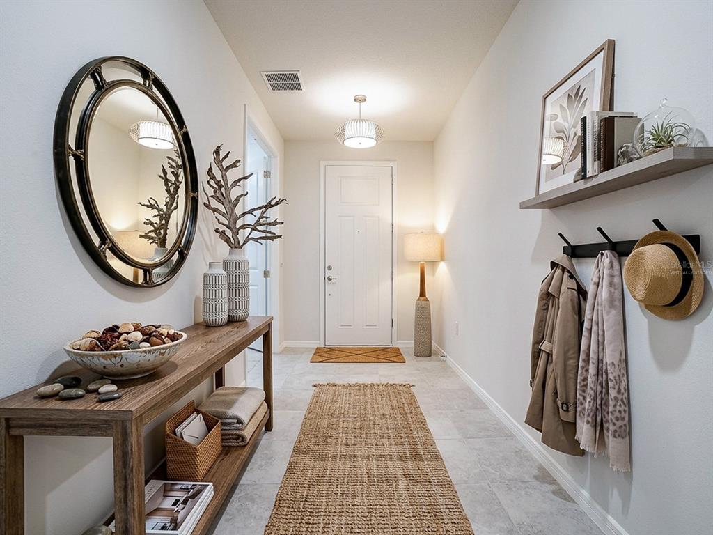 A bright entryway features a console table, a round mirror, a wall shelf, and tile flooring — 7771 SYRACUSE DRIVE, CLERMONT, FL