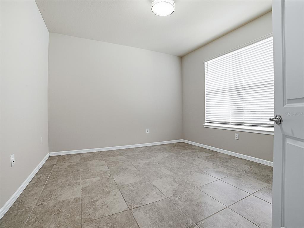 An empty room with light gray walls, tile flooring, a window with blinds, and a ceiling light — 7771 SYRACUSE DRIVE, CLERMONT, FL
