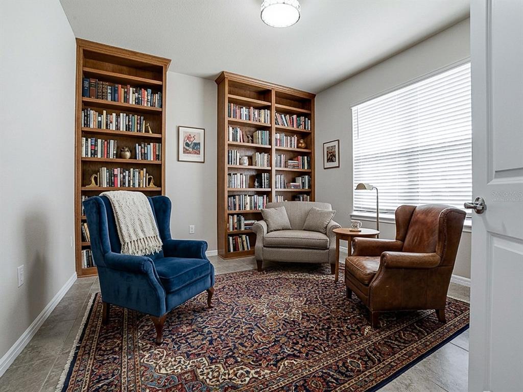 A home library features two wooden bookshelves, three armchairs, and a patterned area rug — 7771 SYRACUSE DRIVE, CLERMONT, FL