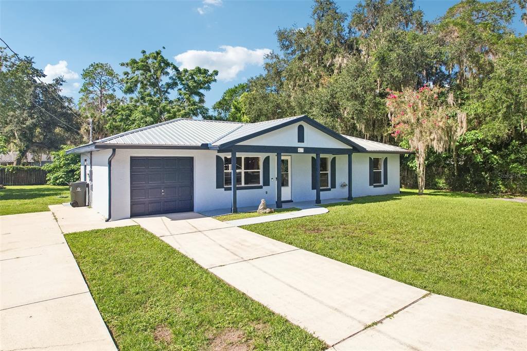 A single-story house with a white stucco exterior, dark trim, and a metal roof — 417 W HUNT AVENUE, BUSHNELL, FL
