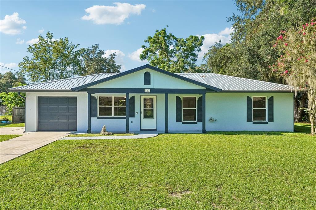A single-story house with a white stucco exterior, dark trim, and a metal roof — 417 W HUNT AVENUE, BUSHNELL, FL