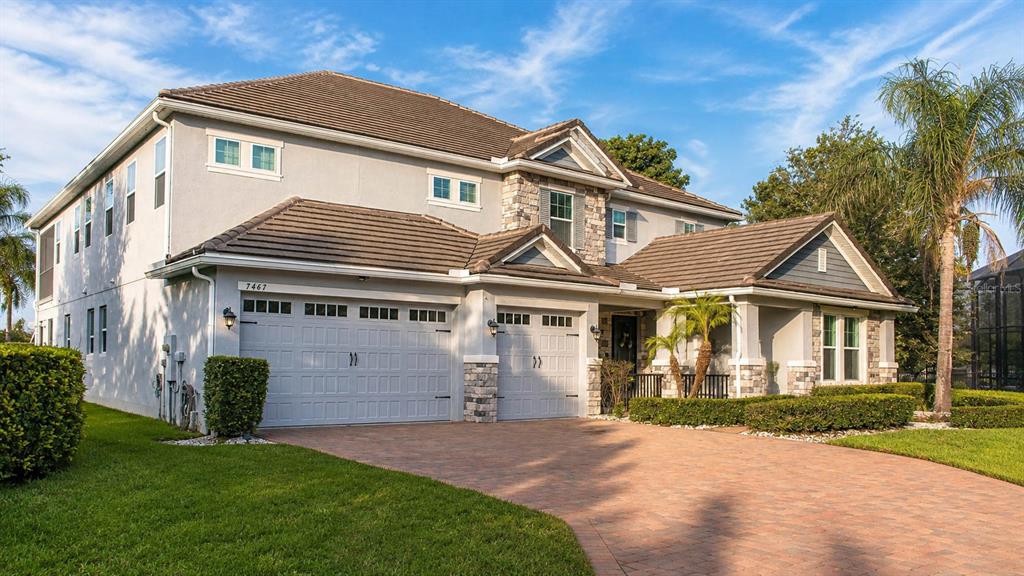 A two-story suburban house with a stone facade, a multi-car garage, and a paved driveway — 7467 LAKE ALBERT DRIVE, WINDERMERE, FL