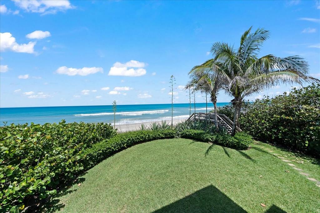 A grassy backyard features a palm tree and a wooden staircase leading to the beach — 5525 HIGHWAY A1A, MELBOURNE BEACH, FL
