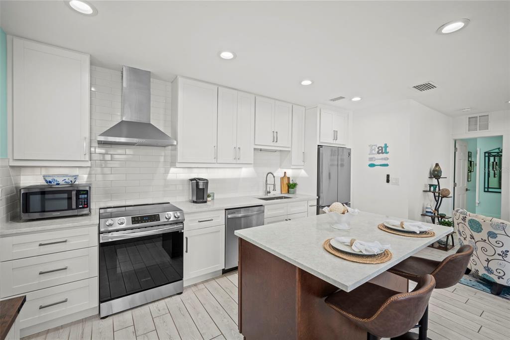 A modern kitchen features white cabinetry, stainless steel appliances, and a dark wood kitchen island — 1841 LAUREL STREET, SARASOTA, FL