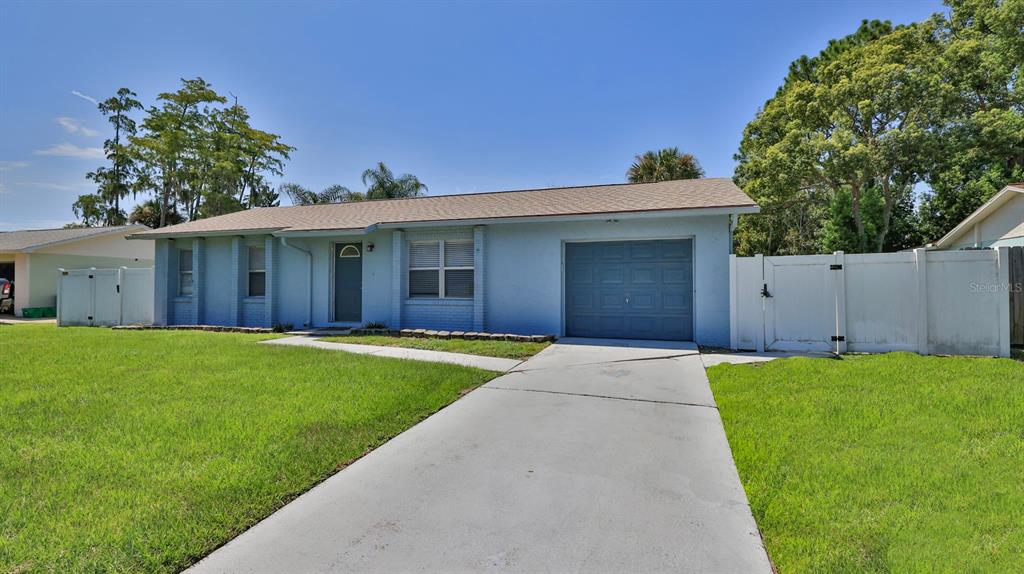 A light blue single-story house features a concrete driveway, a garage, and white vinyl fencing — 1404 N DEXTER DRIVE, PORT ORANGE, FL