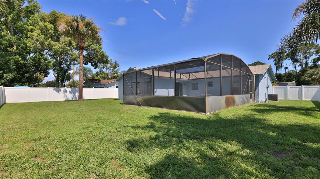 A backyard with a green lawn, a white vinyl fence, and a screened-in pool enclosure — 1404 N DEXTER DRIVE, PORT ORANGE, FL