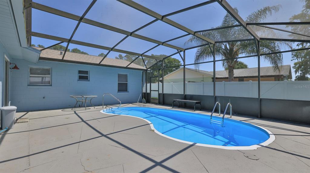 A backyard swimming pool is enclosed by a screened lanai next to a blue house — 1404 N DEXTER DRIVE, PORT ORANGE, FL