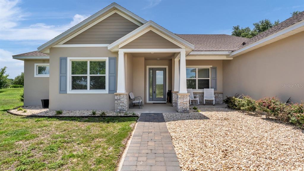 The exterior of a single-story house features a stone-accented porch, a paved walkway, and landscaping — 5701 CRESTVIEW DRIVE, LADY LAKE, FL