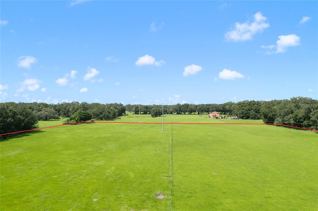 An aerial view shows a large, open green pasture bordered by trees and fencing — CR 552, BUSHNELL, FL