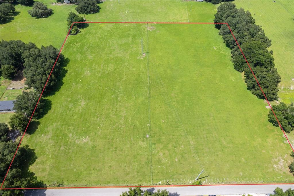 An aerial view shows a large, rectangular grassy lot outlined in red along a road — CR 552, BUSHNELL, FL