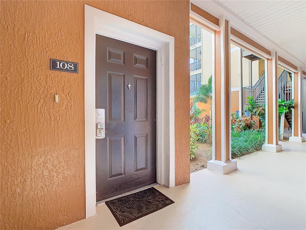 A brown front door labeled 108 is set in a textured orange wall on a walkway — 3050 PIRATES RETREAT COURT UNIT 108, KISSIMMEE, FL