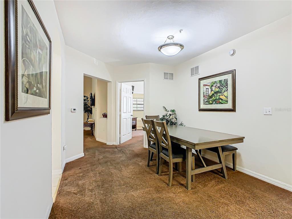 A dining area features brown carpeting, a wooden table with chairs, and wall-mounted artwork — 3050 PIRATES RETREAT COURT UNIT 108, KISSIMMEE, FL