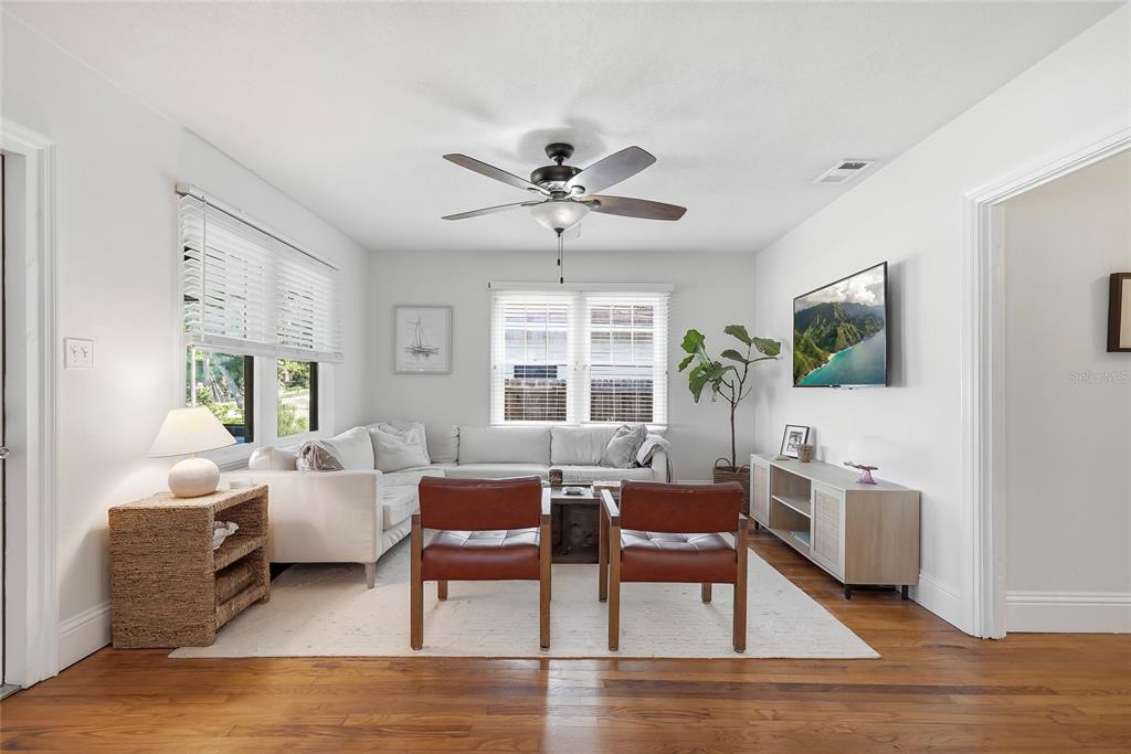 A living room features a white sectional sofa, two leather chairs, and a wall-mounted television — 6031 HOBSON STREET NE, ST PETERSBURG, FL