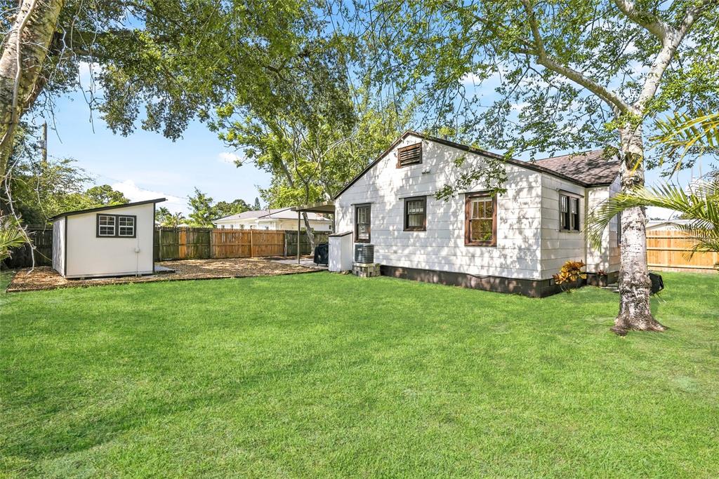 A white house with a detached shed sits in a grassy backyard with mature trees — 6031 HOBSON STREET NE, ST PETERSBURG, FL