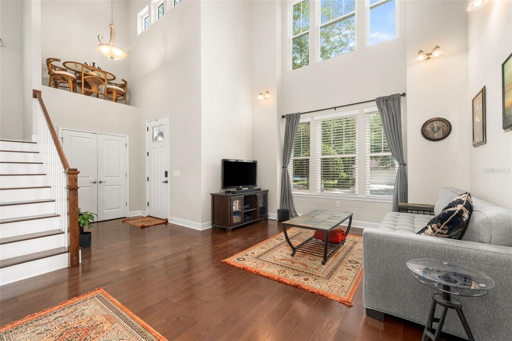 A high-ceilinged living room features hardwood floors, a staircase, and large windows with gray curtains — 8317 SW 78TH LANE, GAINESVILLE, FL