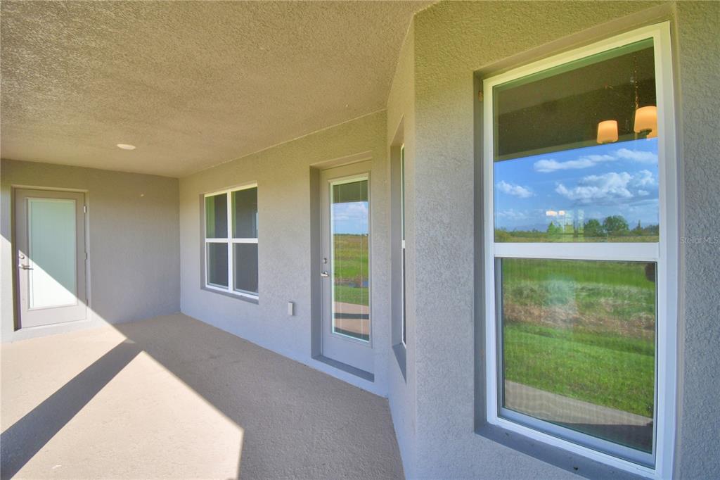A covered outdoor patio with beige stucco walls, two glass doors, and two windows — 4645 CALAMINT LANE, AUBURNDALE, FL