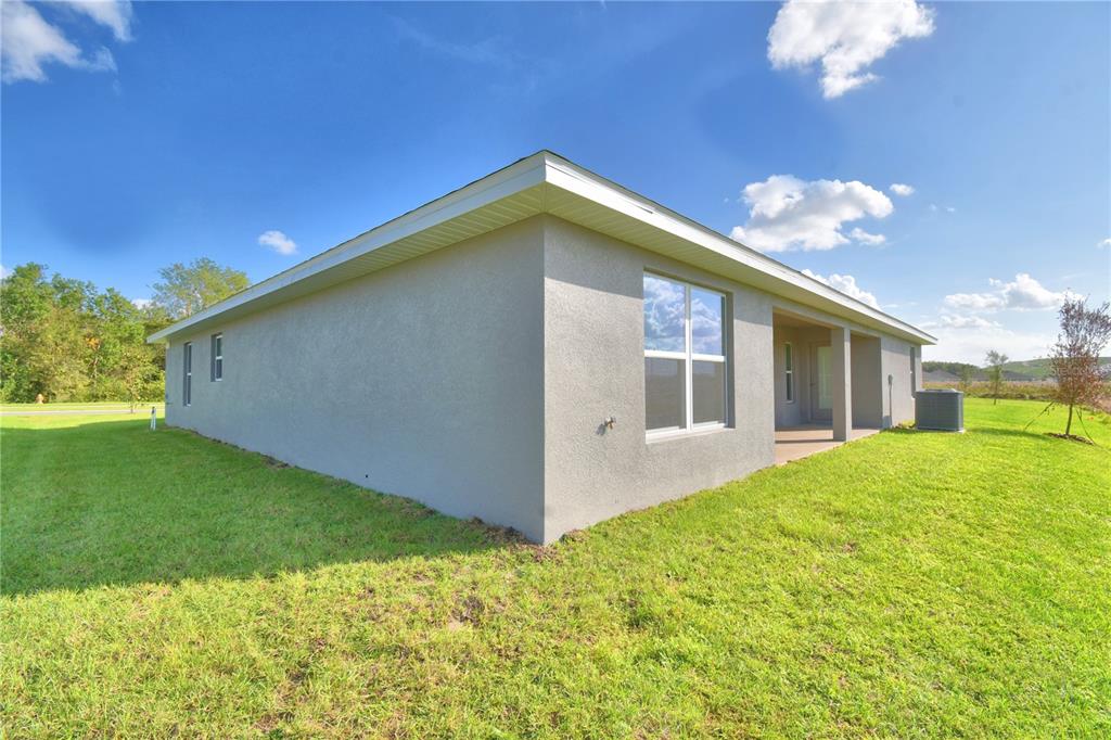 The exterior of a gray stucco house features a covered patio and a grassy yard — 4645 CALAMINT LANE, AUBURNDALE, FL