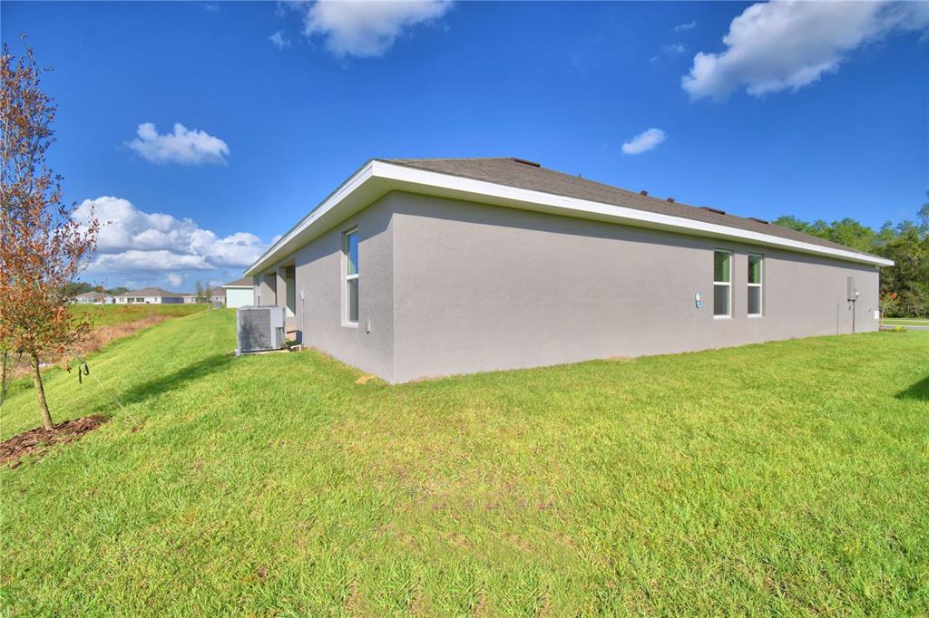 A side view of a gray stucco house with a lawn and an air conditioner unit — 4645 CALAMINT LANE, AUBURNDALE, FL