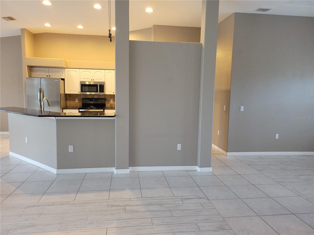 A kitchen with white cabinets and stainless steel appliances overlooks a tiled living area — 9 BUNKER TERRACE, ROTONDA WEST, FL