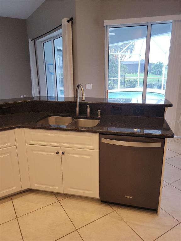 A kitchen features white cabinets, dark granite countertops, a stainless steel dishwasher, and pool views — 9 BUNKER TERRACE, ROTONDA WEST, FL