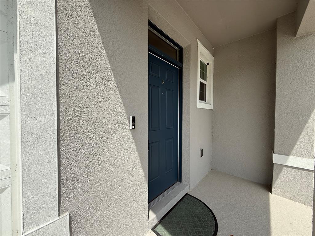 A blue front door is set into a gray stucco exterior wall with a small window — 1503 ISLETA LOOP, KISSIMMEE, FL