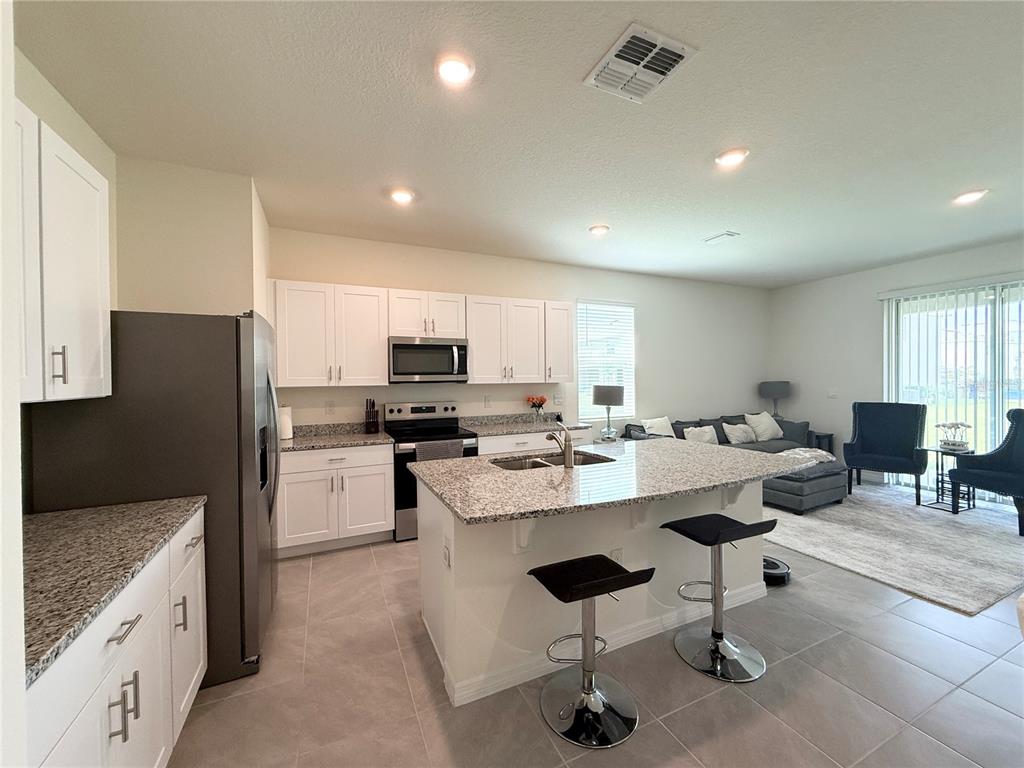 A kitchen with white cabinets, granite countertops, and an island with two bar stools — 1503 ISLETA LOOP, KISSIMMEE, FL