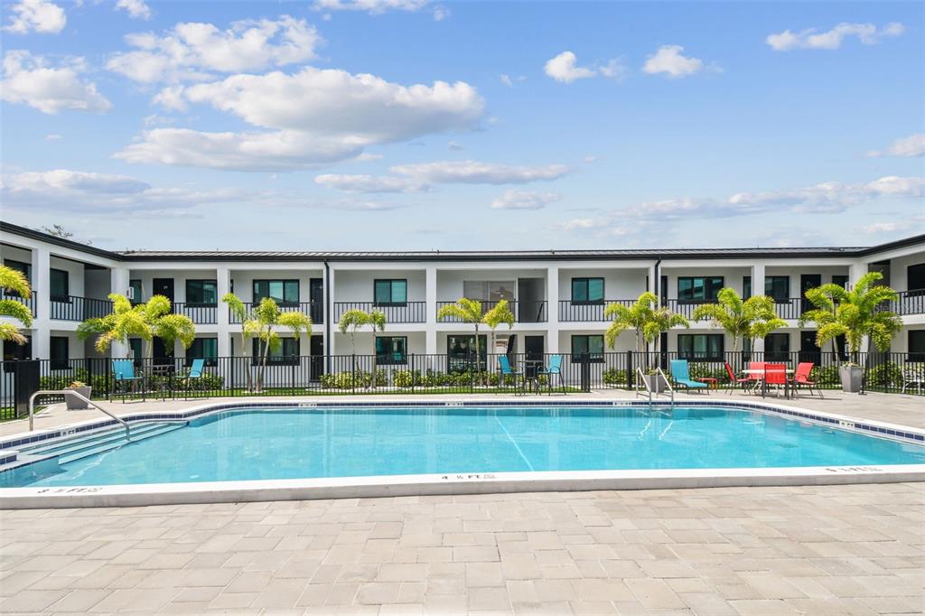 A rectangular swimming pool sits in front of a two-story apartment building with palm trees — 2942 W BAY DRIVE UNIT 22, BELLEAIR BLUFFS, FL