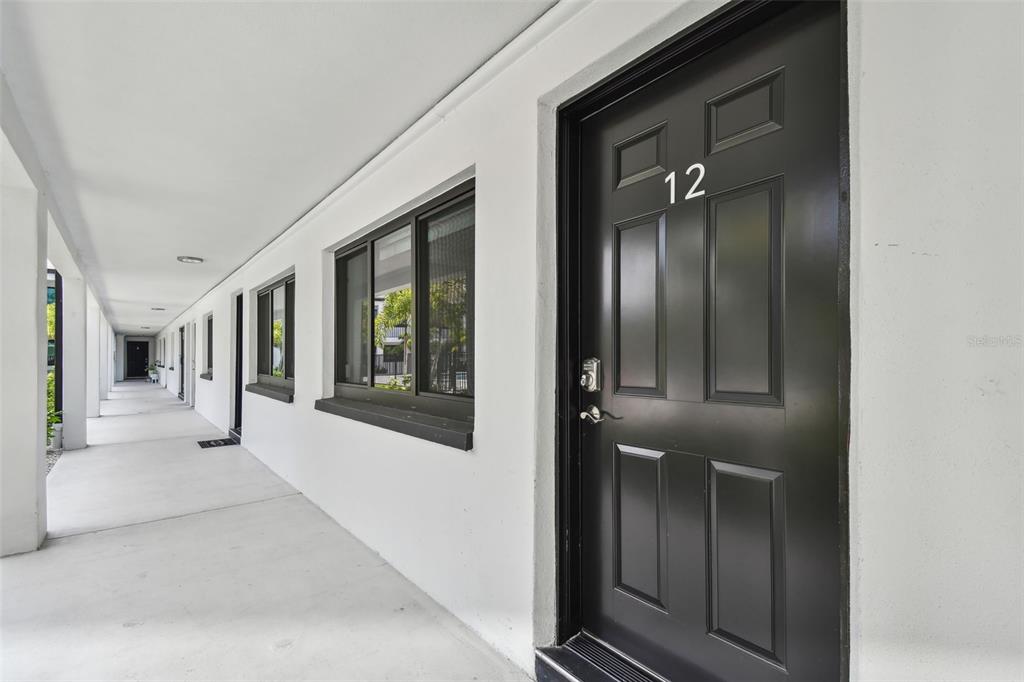 A black front door labeled 12 opens onto a covered outdoor walkway with white walls — 2942 W BAY DRIVE UNIT 22, BELLEAIR BLUFFS, FL