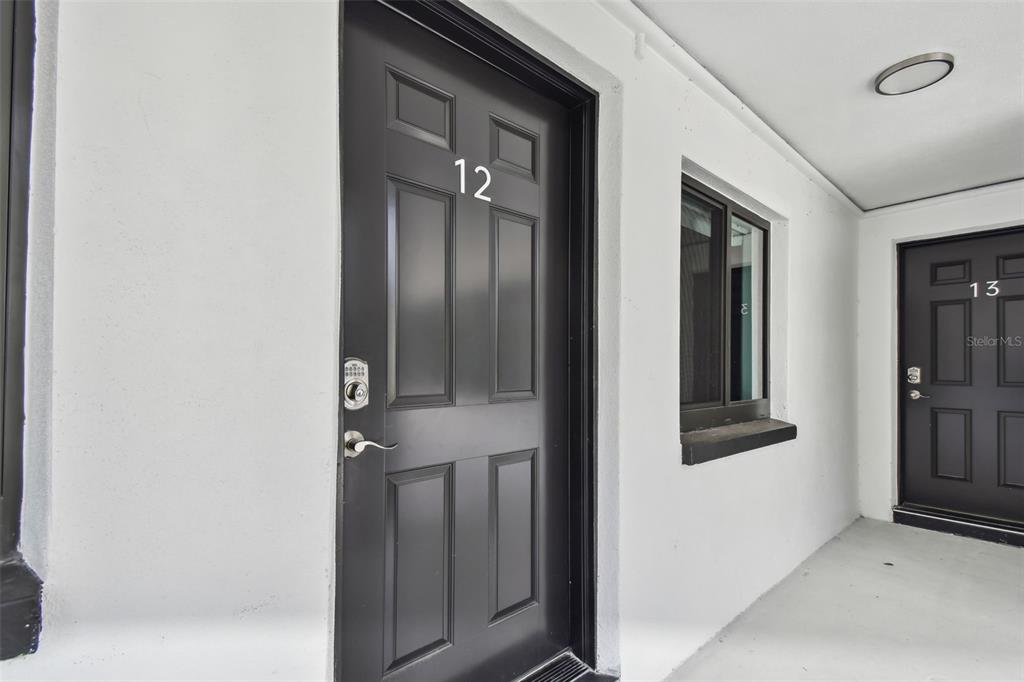 Two black apartment doors labeled 12 and 13 are set into a white exterior wall — 2942 W BAY DRIVE UNIT 22, BELLEAIR BLUFFS, FL