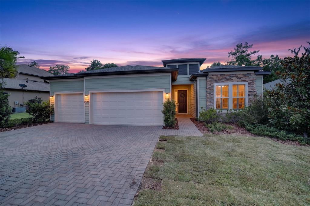 A single-story house with a three-car garage, stone accents, and a paved driveway at dusk — 4310 SE 11TH AVENUE, OCALA, FL