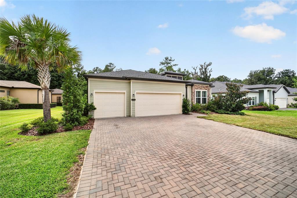 A light green house with a three-car garage and a paved driveway under a blue sky — 4310 SE 11TH AVENUE, OCALA, FL
