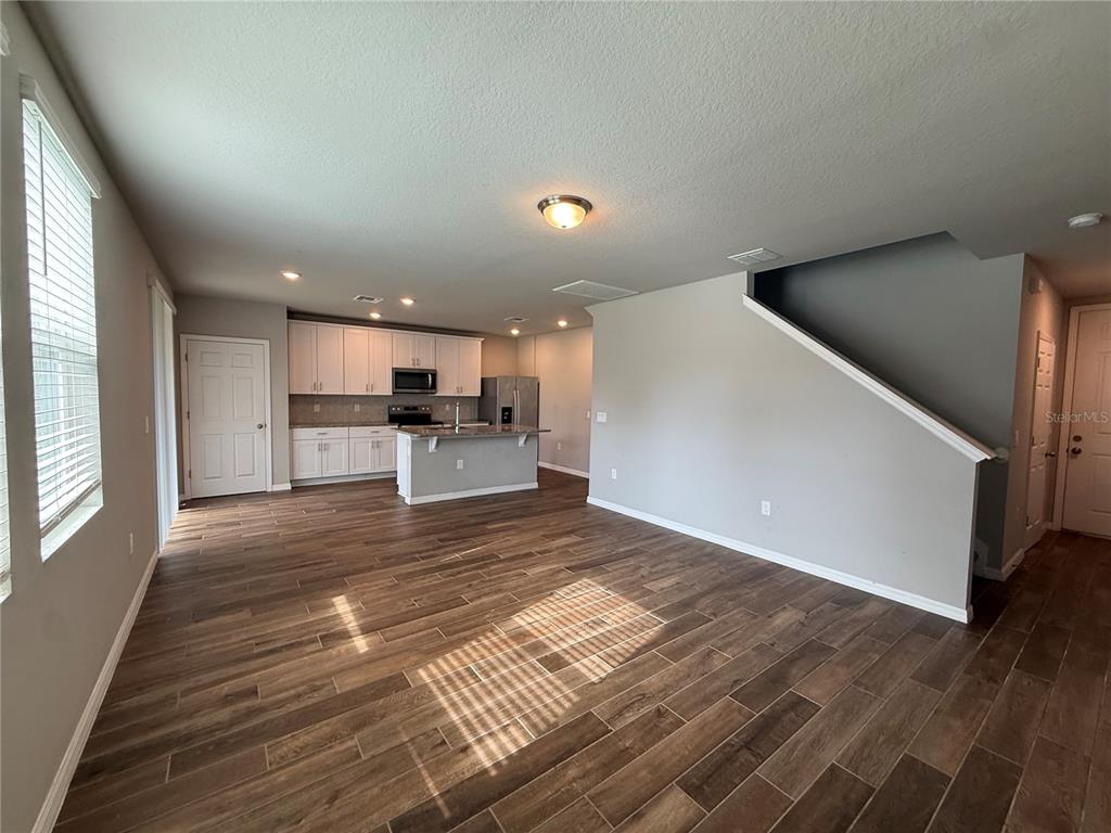 An open-concept kitchen and living area feature wood-look tile flooring and a staircase — 5264 STEPHS FIELD STREET, ST CLOUD, FL