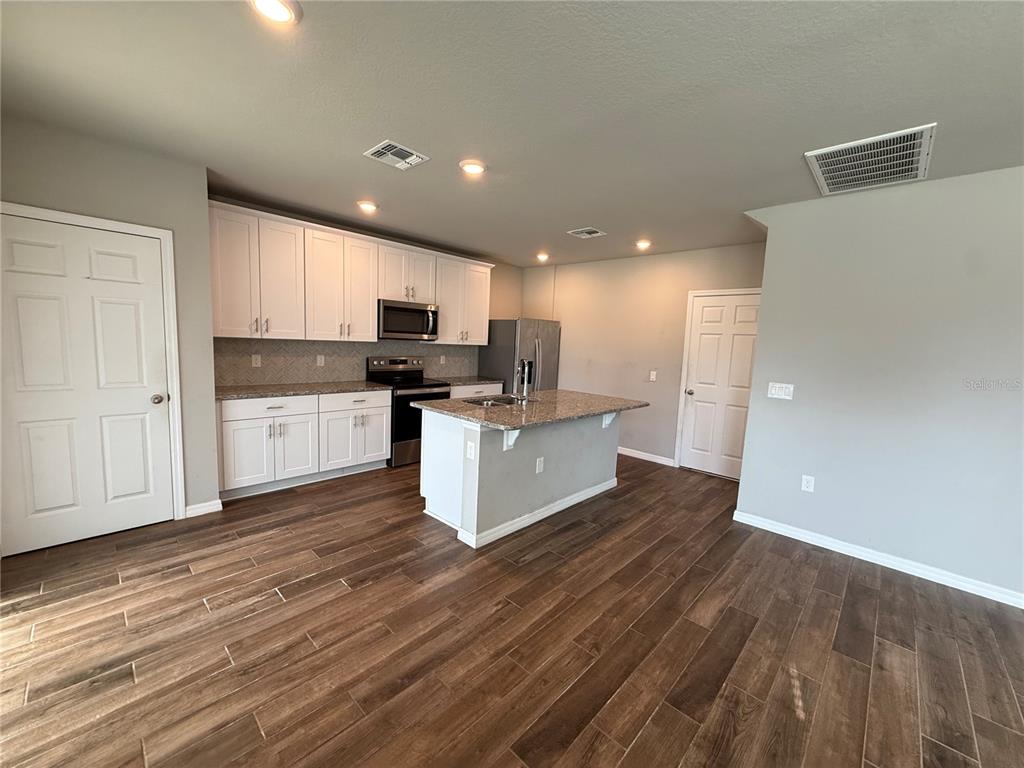 A kitchen features white cabinetry, granite countertops, a center island, and wood-look tile flooring — 5264 STEPHS FIELD STREET, ST CLOUD, FL