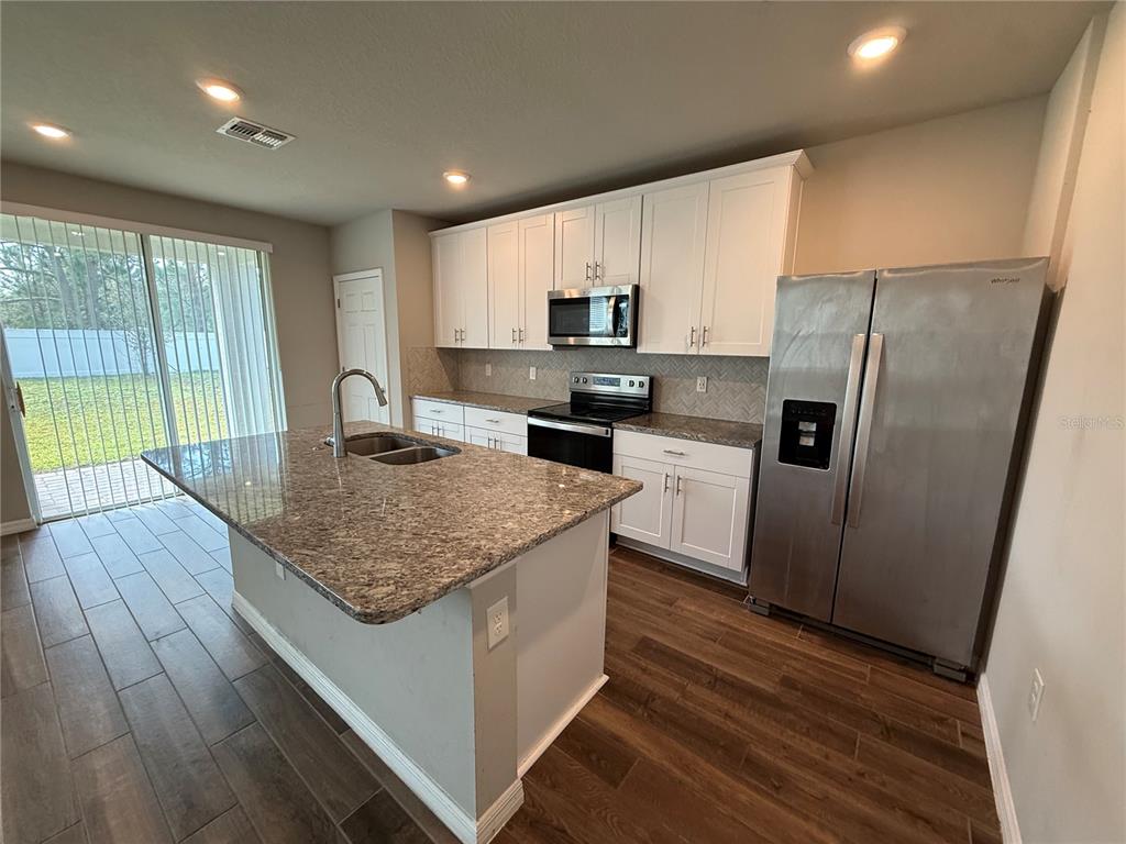 A kitchen features white cabinets, granite countertops, a center island, and stainless steel appliances — 5264 STEPHS FIELD STREET, ST CLOUD, FL