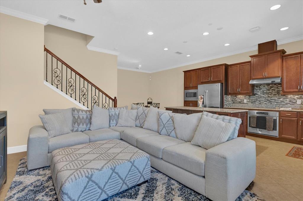 A living room with a large sectional sofa faces an open kitchen with wooden cabinets — 9219 LAUREATE BOULEVARD, ORLANDO, FL